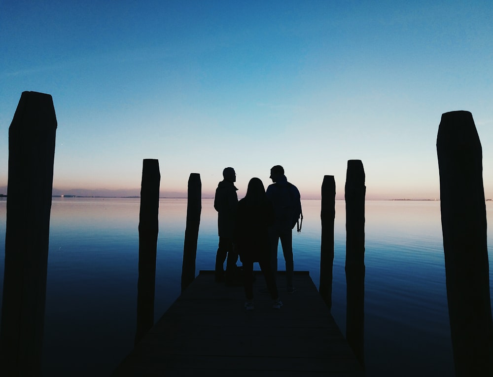 silhouette of three person on seadock