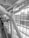 A large structural beam is prominently featured, intricately designed and bolted in an architectural space. The environment includes large glass windows allowing natural light to flood into the space. Several people are using an escalator, ascending or descending, adding a sense of movement to the scene.