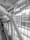 A large structural beam is prominently featured, intricately designed and bolted in an architectural space. The environment includes large glass windows allowing natural light to flood into the space. Several people are using an escalator, ascending or descending, adding a sense of movement to the scene.