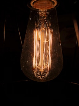 A close-up of a glowing vintage-style filament light bulb casting a warm amber light.