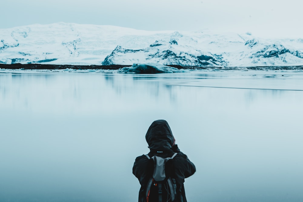 person viewing calm body of water and snow capped mountain