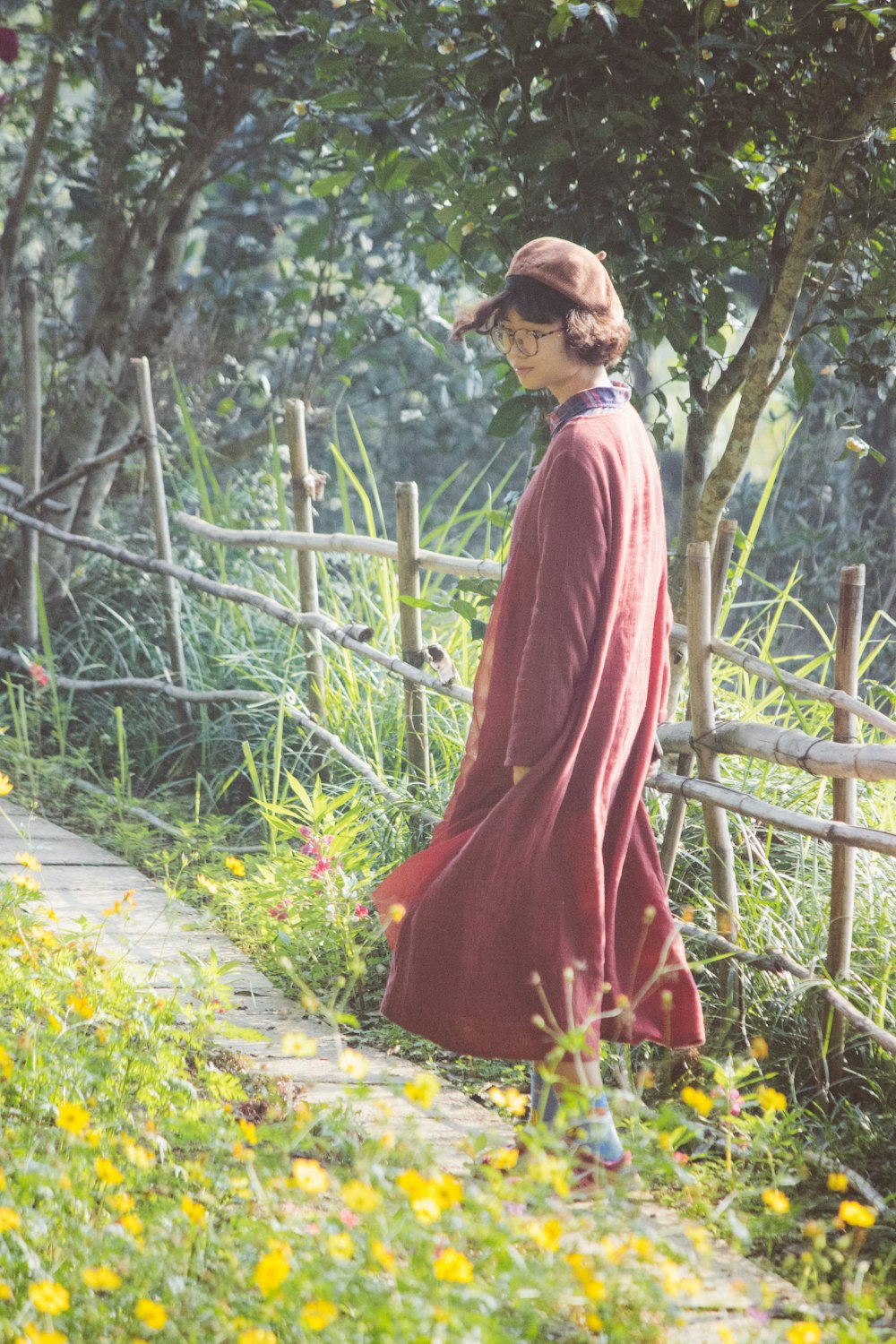 woman in long red coat walking on pathway at the garden