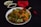 A bowl of tantalizing Indian rice and meatball dish garnished with fresh herbs and green onions. The dish is accompanied by two small bowls, one containing green chilies and the other a dark sauce, placed on a dark surface. Additionally, there is a red cloth napkin with a bamboo-themed chopstick set placed next to the bowl.