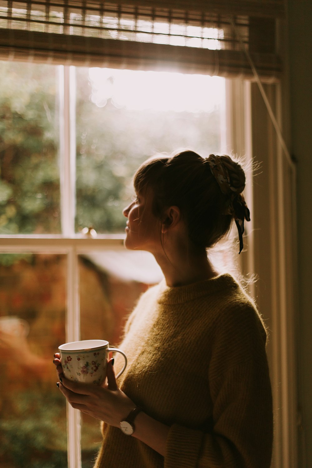 昼間、部屋の窓際に立ちながら茶碗を持つ女性