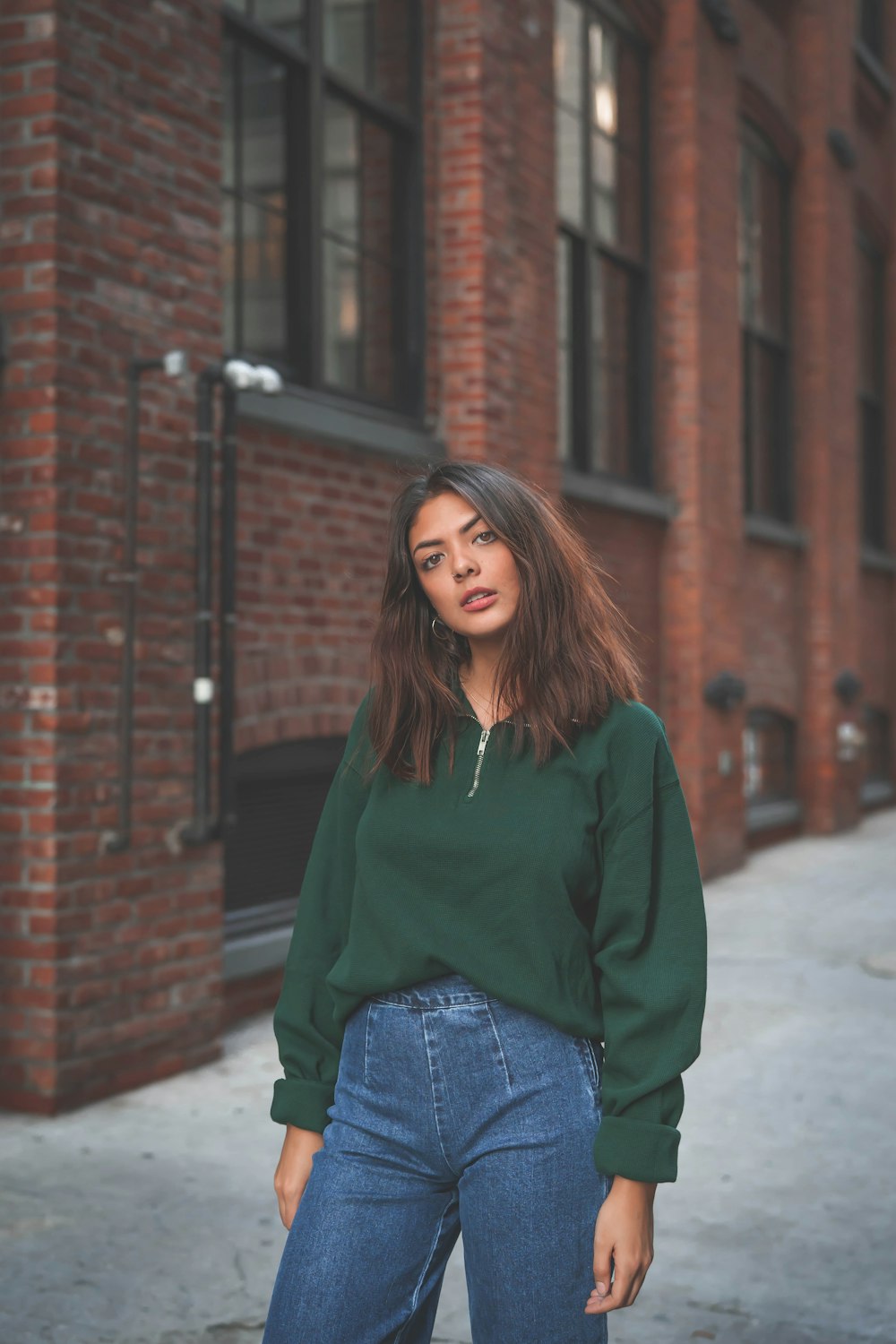 woman in green sweater and blue pants by buildingg