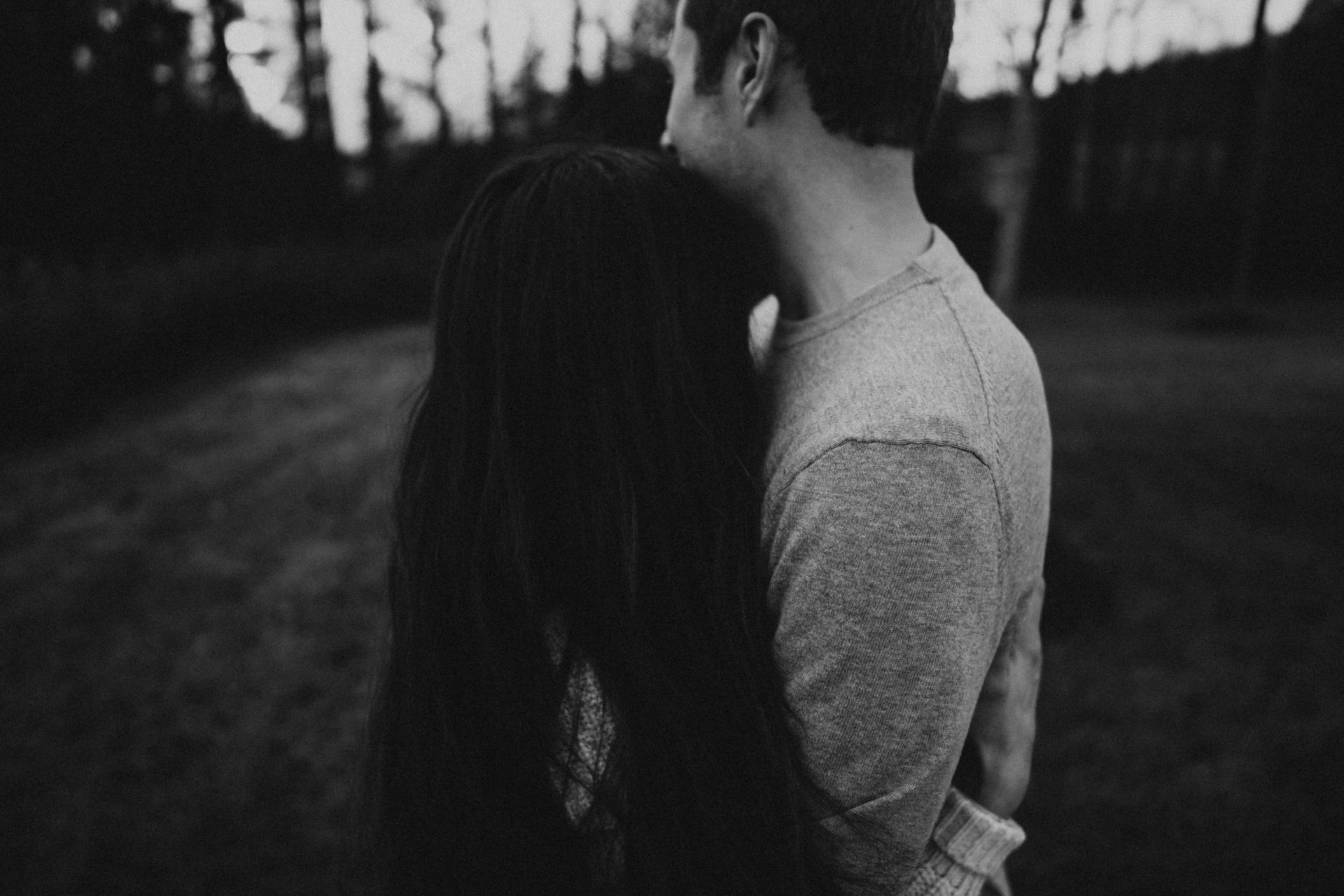 An intimate black-and-white photo of an engaged couple sharing a quiet, tender moment outdoors.