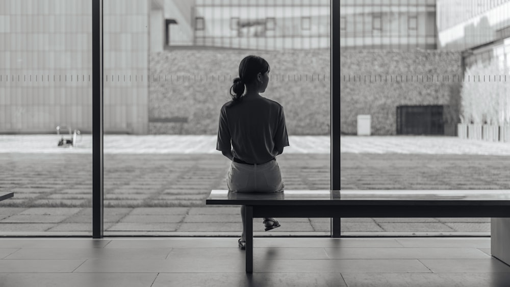 woman sitting on bench in greyscale photography