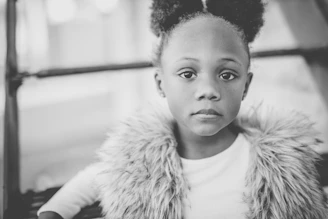 An editorial-style photograph of a child dressed in refined, minimalist luxury clothing against a soft beige backdrop.