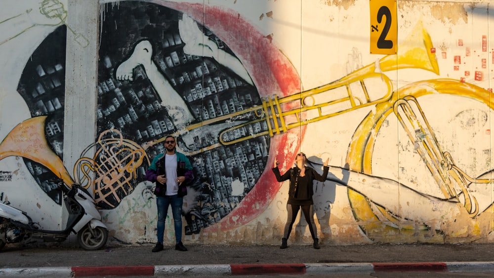 man and woman standing near wall with music instrument graffiti