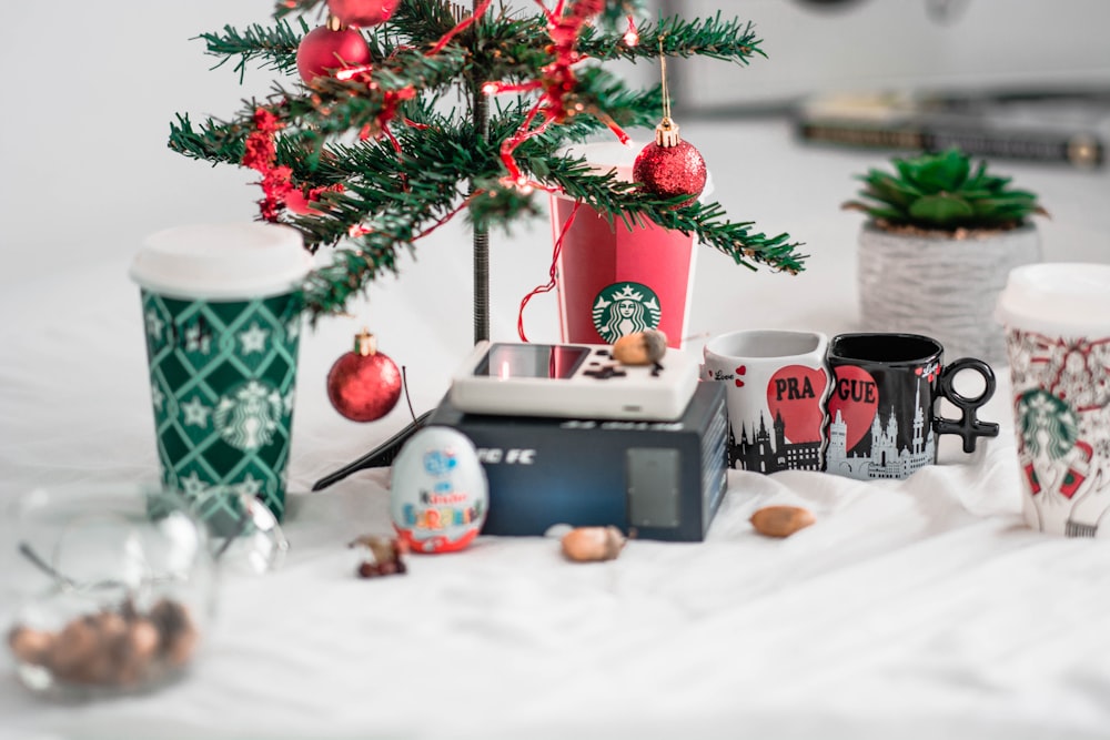 two ceramic mugs beside two cups and christmas tree