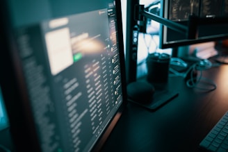 Several computer monitors display various screens with digital content, including text and graphics. A keyboard is visible on the desk, along with a smart speaker and some cables. The lighting is dim, suggesting a work or gaming setup.