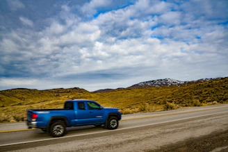A sleek dark blue truck driving on a sunlit European highway with mountains in the background.