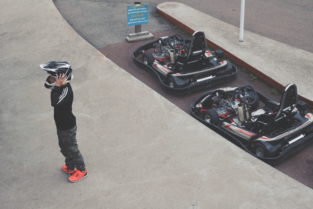 person wearing helmet standing beside two go-karts