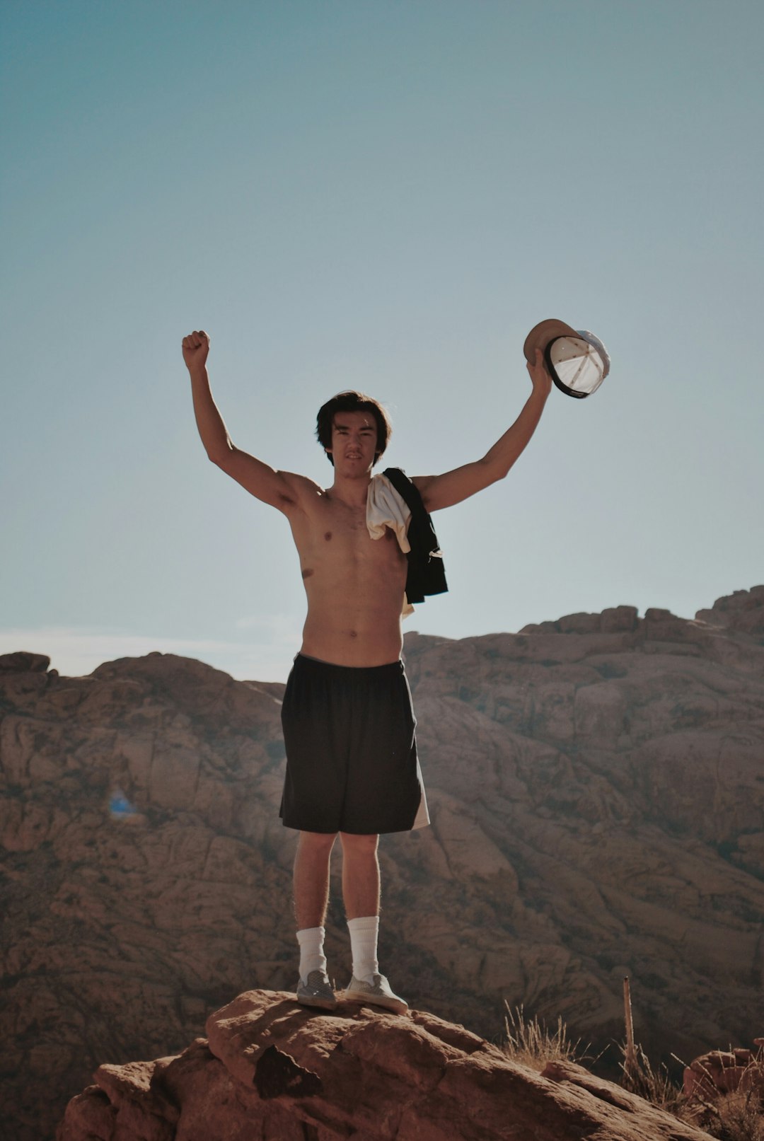 topless man stands on brown rock mountain edge]