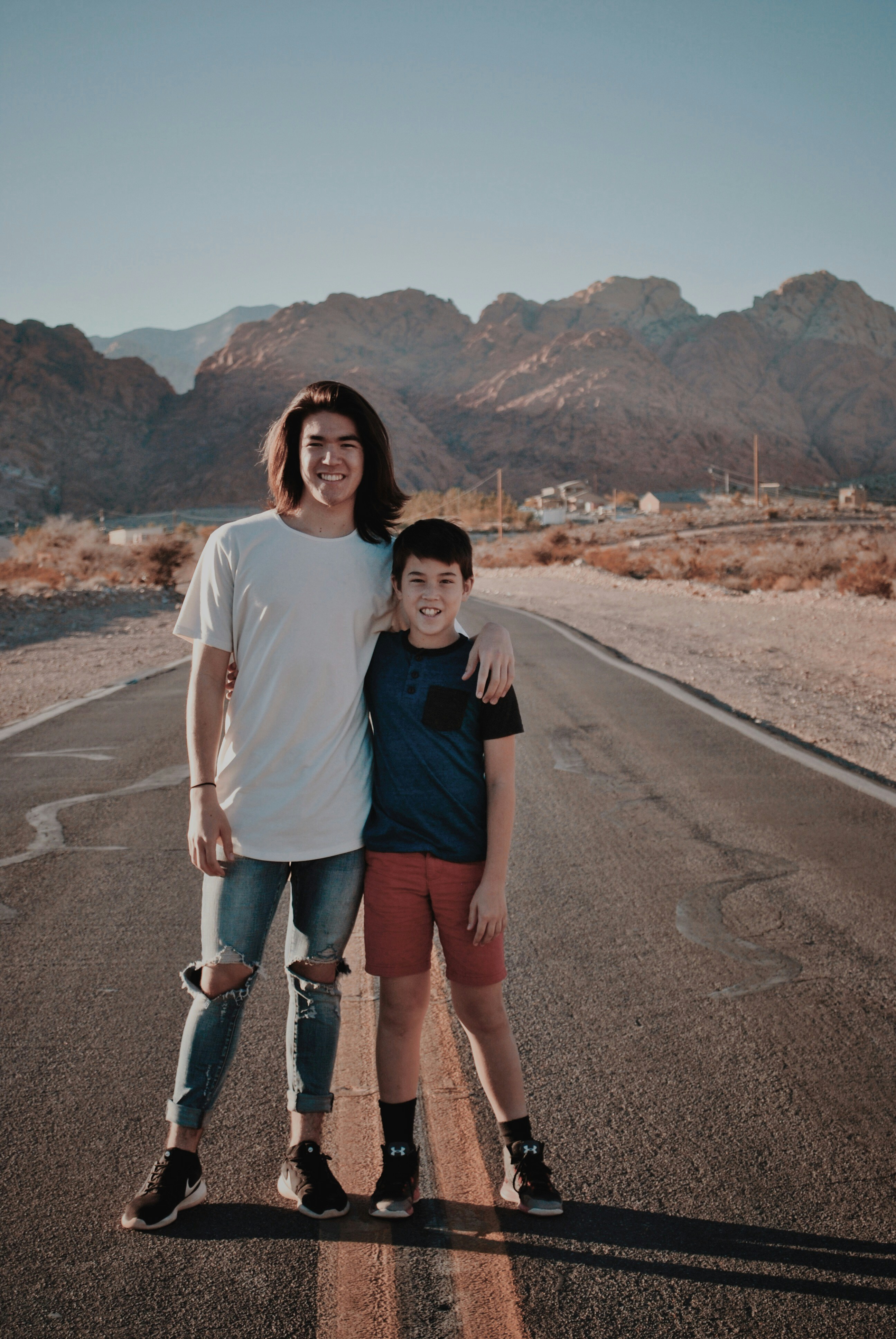 person wearing blue ripped jeans besides boy wearing blue shirt standing on asphalt road during daytime