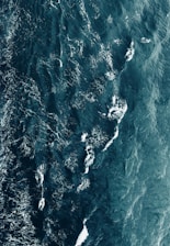 Aerial view of deep blue ocean waters with visible waves and white foam patterns creating intricate designs across the surface.