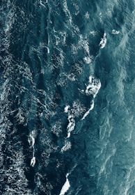 Aerial view of deep blue ocean waters with visible waves and white foam patterns creating intricate designs across the surface.