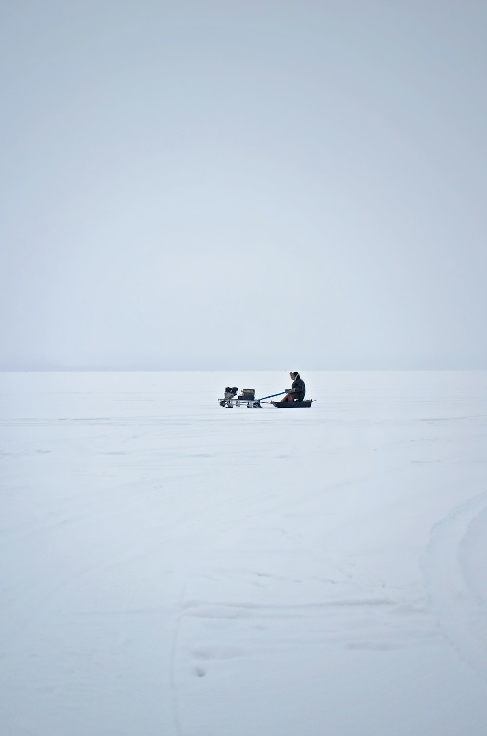 Mann fährt mit gezogenem Schlitten mitten auf einem verschneiten Feld