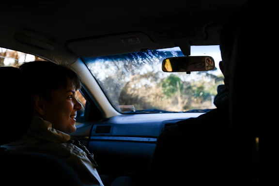 A friendly driver assisting a passenger into a clean, modern vehicle in a sunny Kissing street.