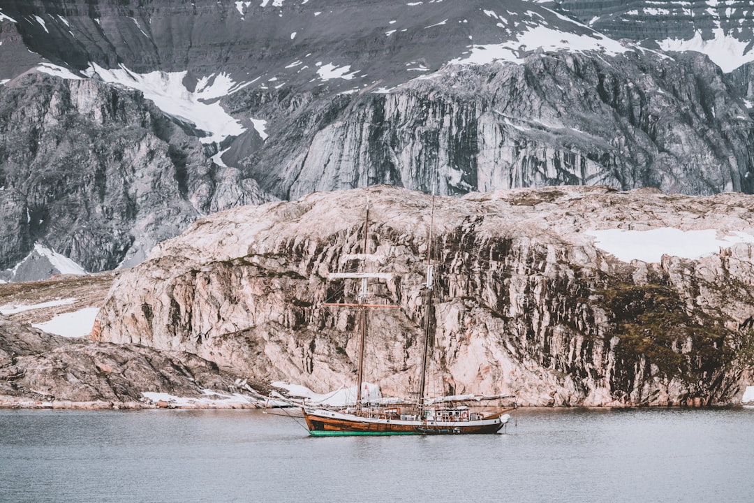 brown and white boat on calm water front of mountain