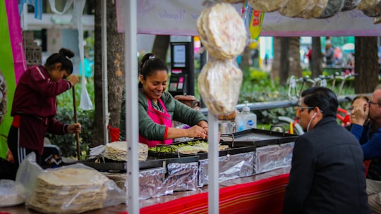 Close-up of a smiling vendor handing a freshly prepared meal to a customer outdoors.