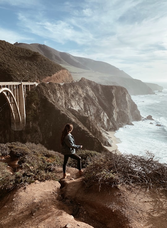 woman standing on top of mountain looking at sea in Bixby Creek Arch Bridge United States