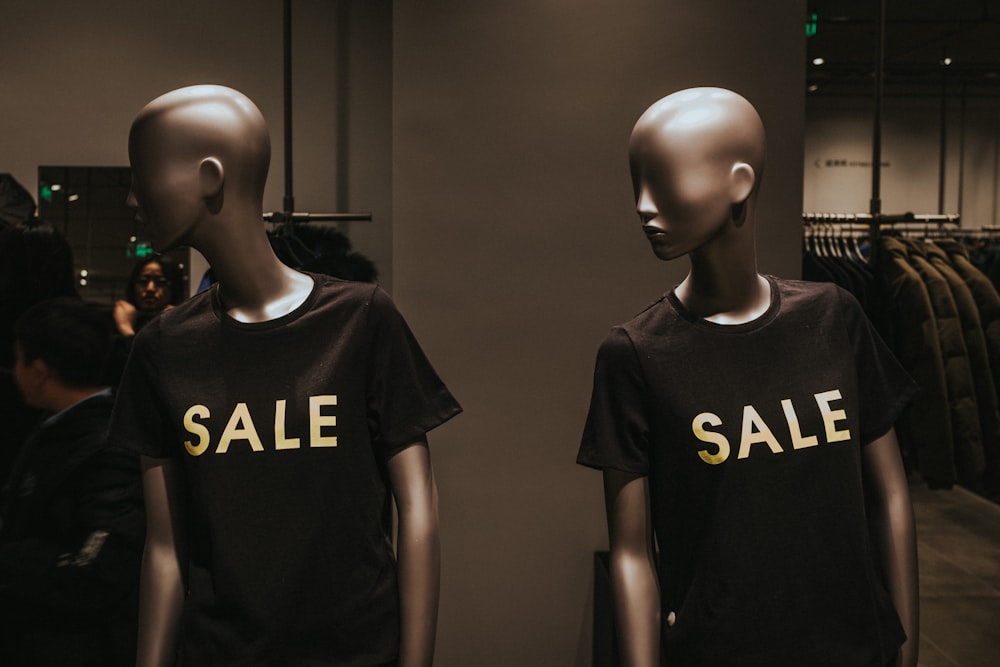 dos maniquíes con camisetas negras de cuello redondo con estampado de Sale