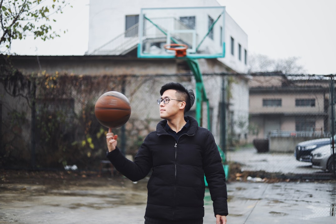 man wearing black bubble zip jacket with basketball spinning on his right index finger