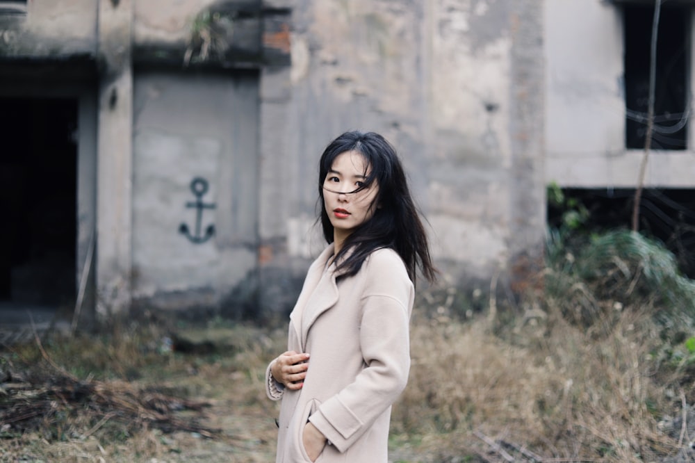 woman wearing beige coat standing near building ruins