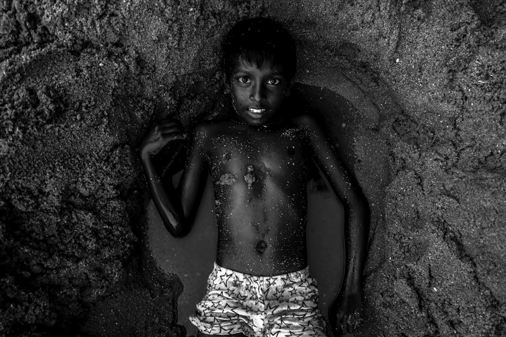Graustufenfotografie eines Oben-ohne-Jungen, der auf nassem Sand liegt