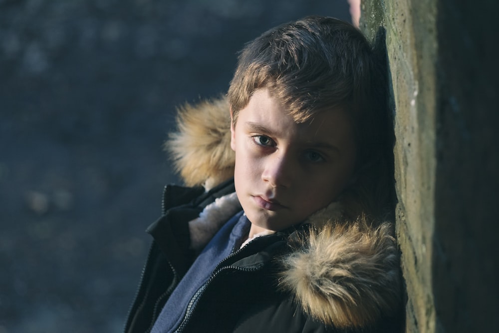 boy wearing coat leaning on wall