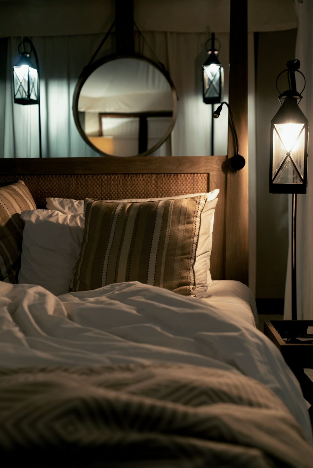 침대에 여러 가지 빛깔의 베개와 방 안에 조명이 켜진 펜던트 램프
