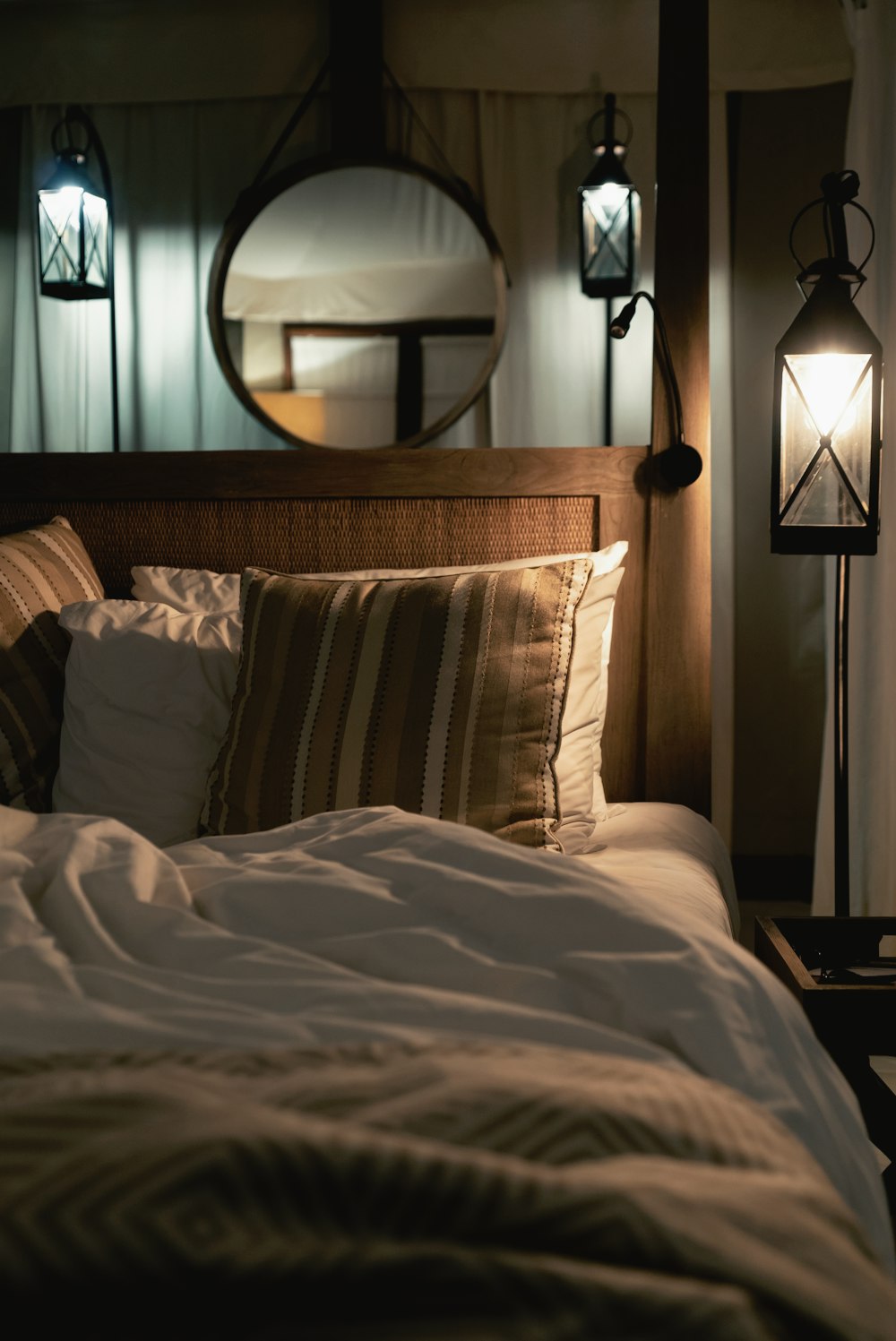 침대에 여러 가지 빛깔의 베개와 방 안의 조명이 켜진 펜던트 램프