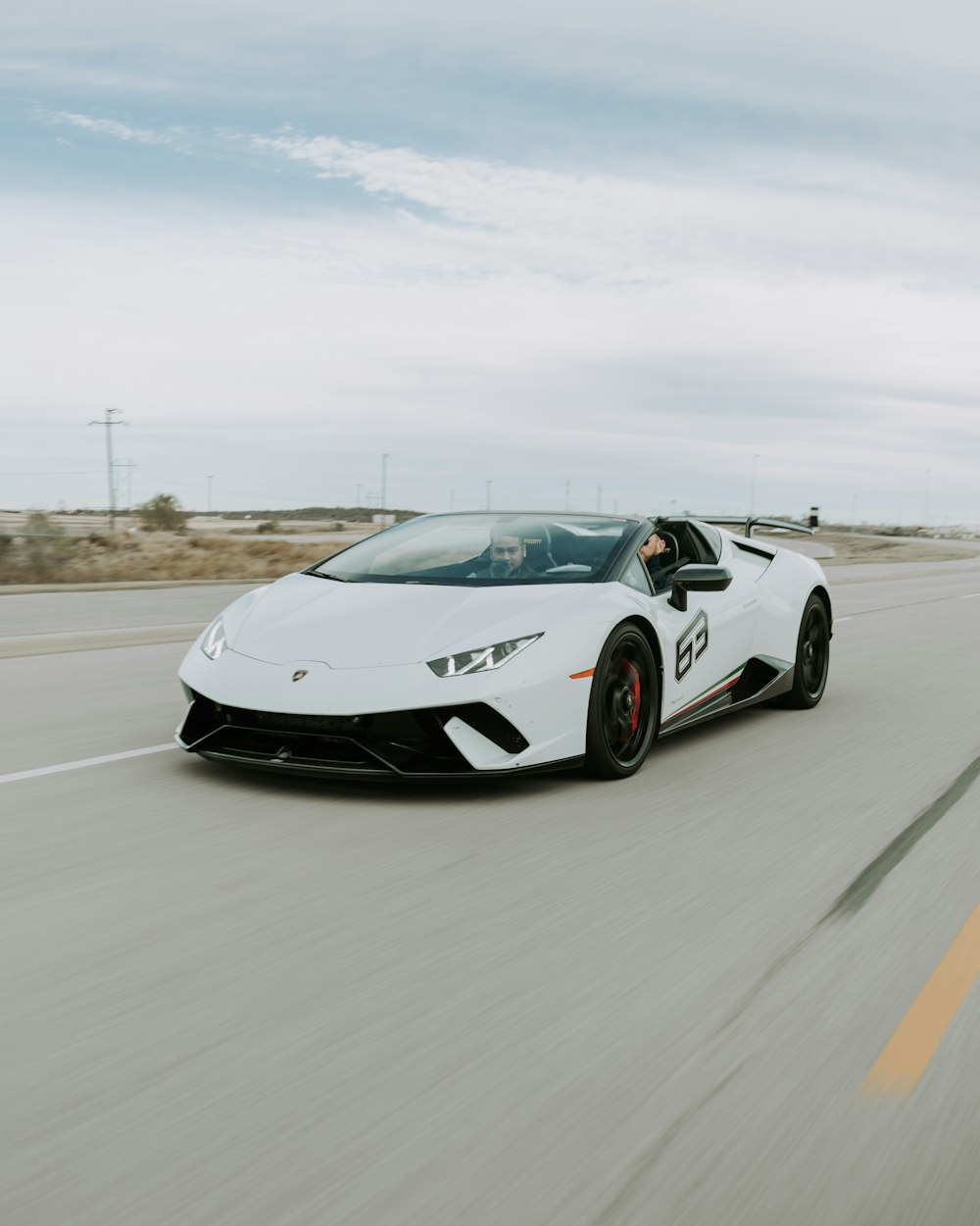 deux hommes conduisant une Lamborghini Huracan Spyder blanche pendant la journée