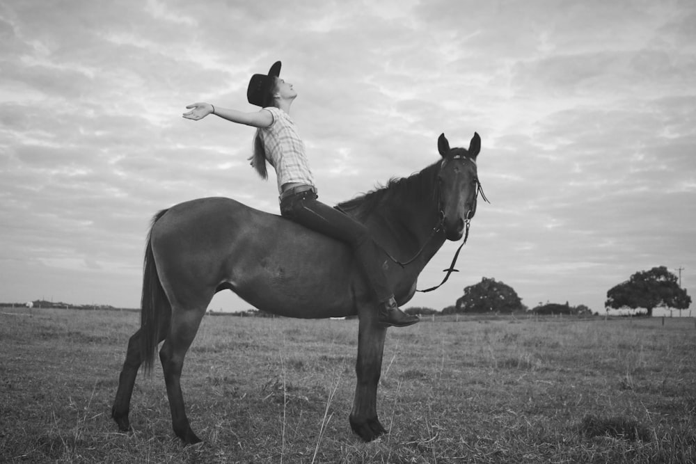 fotografia em tons de cinza da mulher montando cavalo no campo da grama