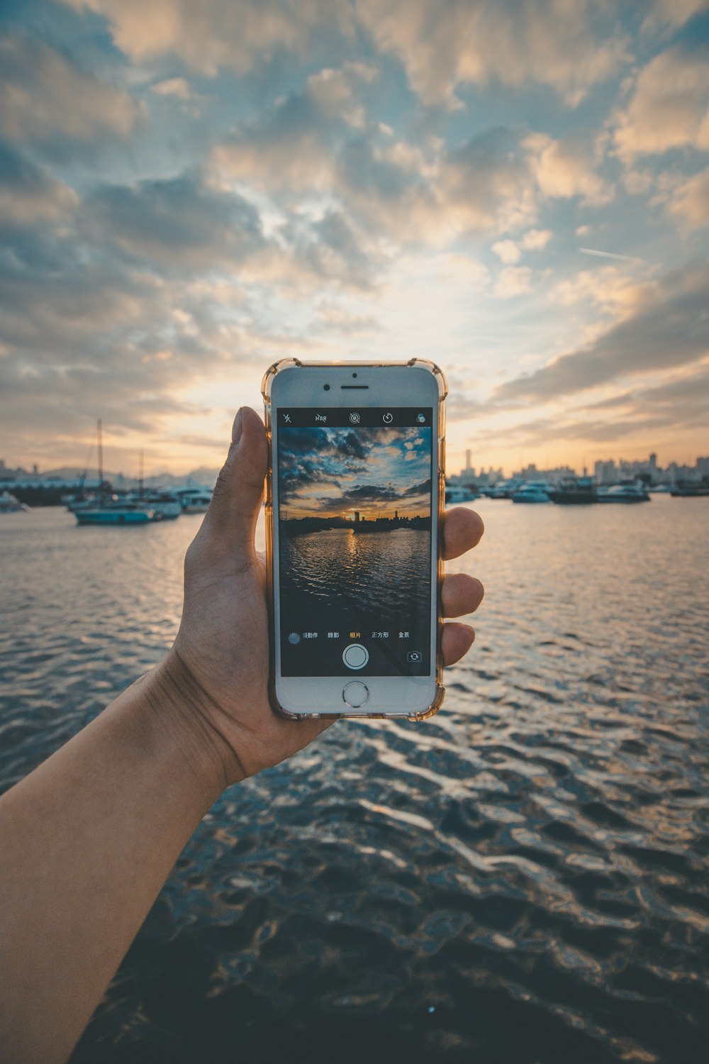 gold iPhone 6 held over the water at harbor