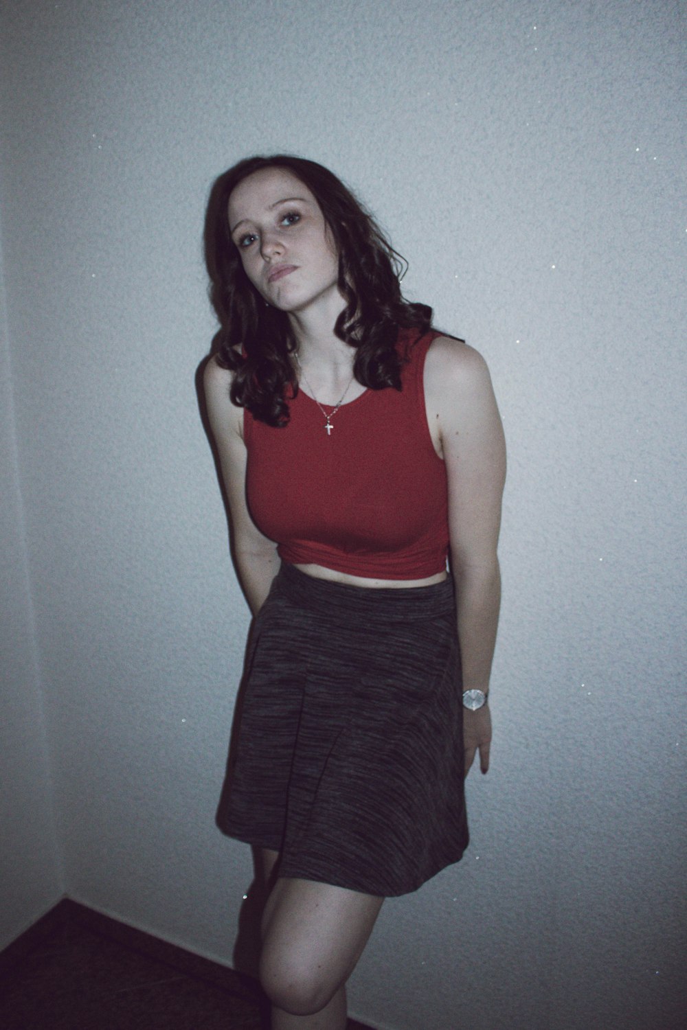 woman wearing red top and gray skirt leaning on wall