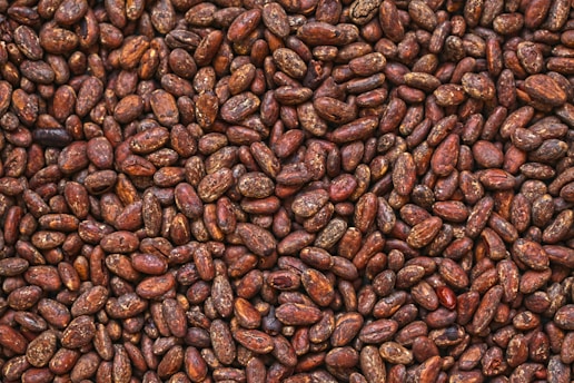 A close-up view of numerous brown cocoa beans densely packed together, displaying variations in shades and textures.