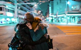 A couple exchanging warm embraces in a city street lit by twinkling evening lights.
