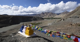 A scenic landscape with mountains in the background, a river flowing through the valley, and colorful prayer flags fluttering in the wind next to brightly painted stupas.