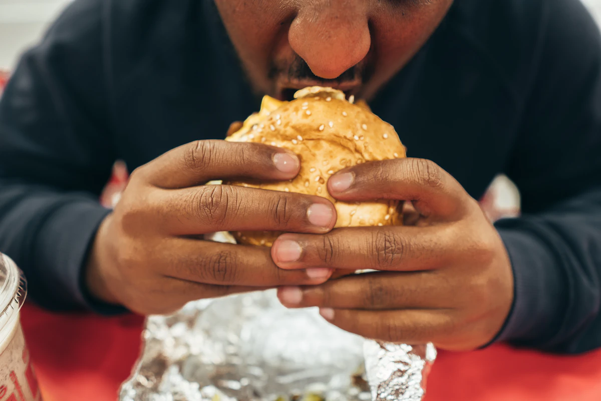 Man taking a large bite of a fast-food hamburger, illustrating dietary choices that can lower testosterone.