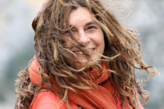 Smiling woman wearing a bright scarf outdoors on a breezy day.