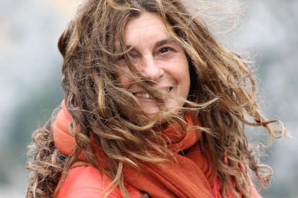 Smiling woman wearing a bright scarf outdoors on a breezy day.