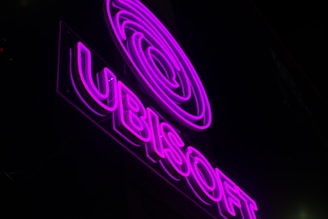 A neon sign with glowing purple lights displaying the logo and name Ubisoft against a dark background. The bright, vivid colors contrast sharply with the darkness around it.