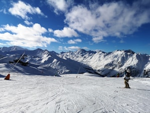 A panoramic view of snow-covered Alpine mountains with skiers descending a crisp, sunny slope.