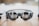 A pair of sleek, modern augmented reality glasses with large round lenses and multiple small cameras on the frame, placed on a wooden table. The design is minimalistic and high-tech, with a focus on functionality and innovation.