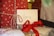 A close-up view of holiday-themed presents, featuring red wrapping paper with white snowflake patterns and white twine. An envelope with the word 'love' written in glittery letters is placed on top. A red ribbon is tied around another present, and additional cards are visible in the background.