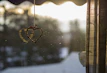 Close-up of a colorful ceramic heart ornament hanging by a window, catching the morning light.
