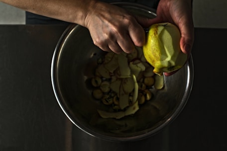 Close-up of hands using a sleek vegetable peeler over a fresh salad bowl