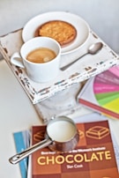 A rustic wooden table set with a steaming cup of coffee and a small bowl of rich cacao nibs.